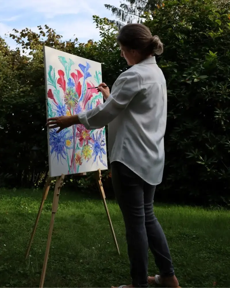 Femme peignant une toile colorée représentant des fleurs, en plein air, dans un jardin | Coralie channeling art