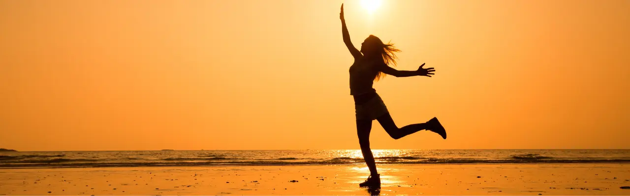 Silhouette d'une femme sautant de joie sur une plage au coucher du soleil, symbolisant la clarté mentale et la réussite d'un changement de vie.